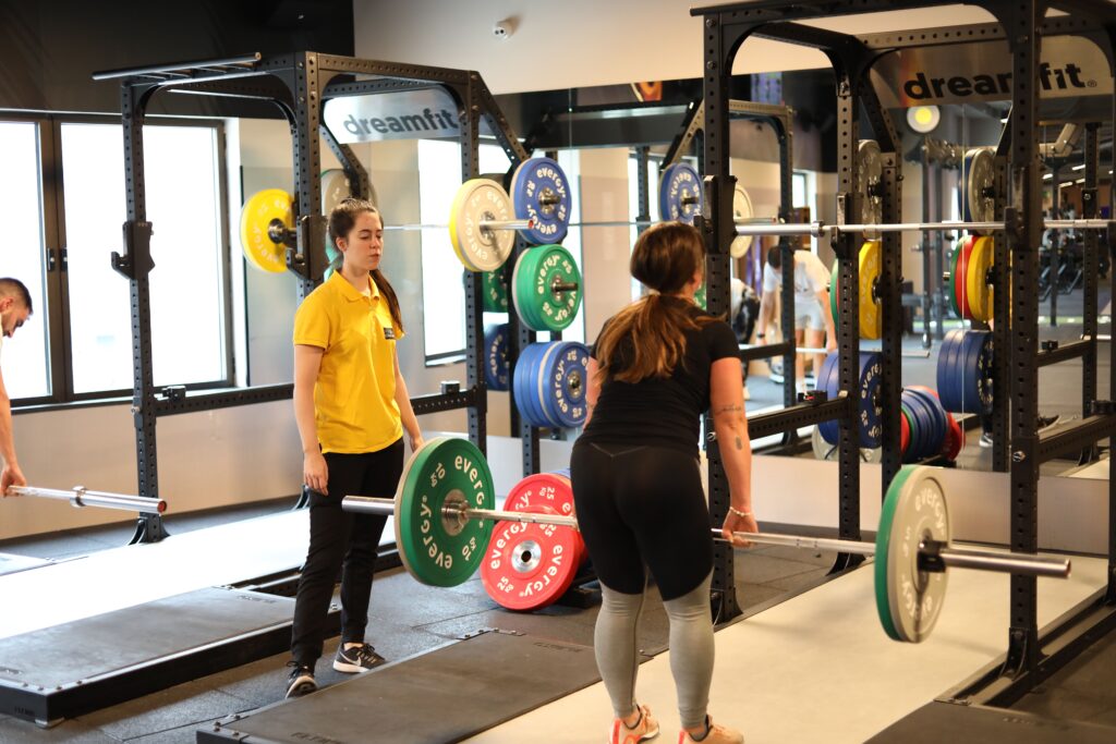 Two women weightlifting in a modern gym with colorful plates, showcasing fitness training.