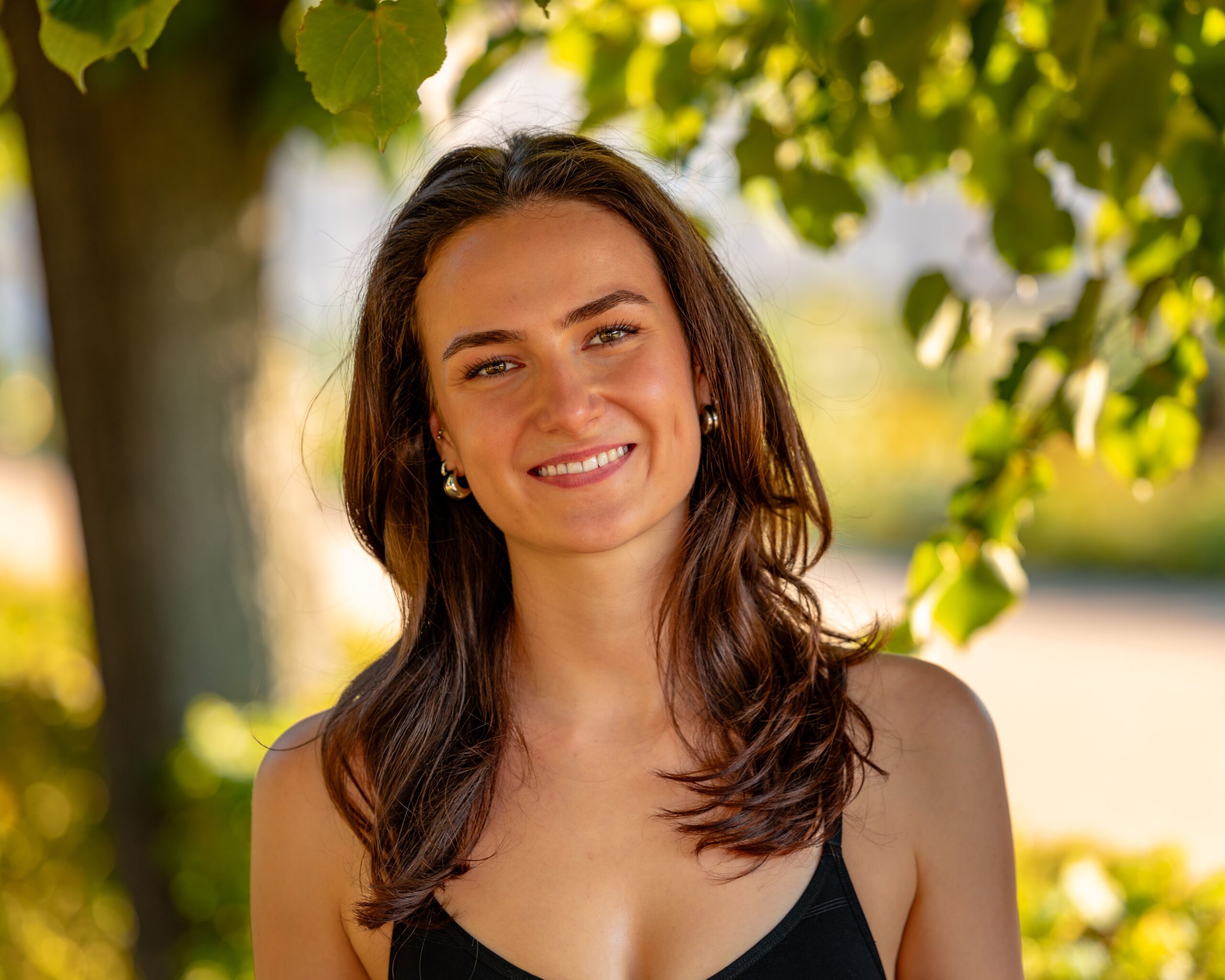 Portrait of a smiling woman enjoying a sunny day outdoors under a tree in Berlin.